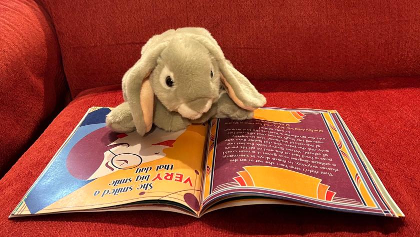 Sprinkles is reading Beautiful Symmetry: The Story of Emmy Noether, written by Jessica Christianson and illustrated by Brittany Goris.
